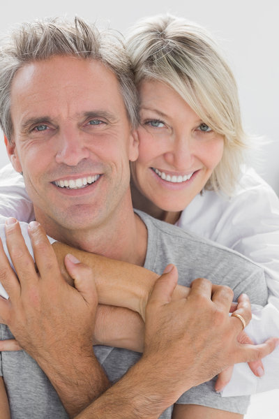 Hugging couple smiling at camera at home in bedroom